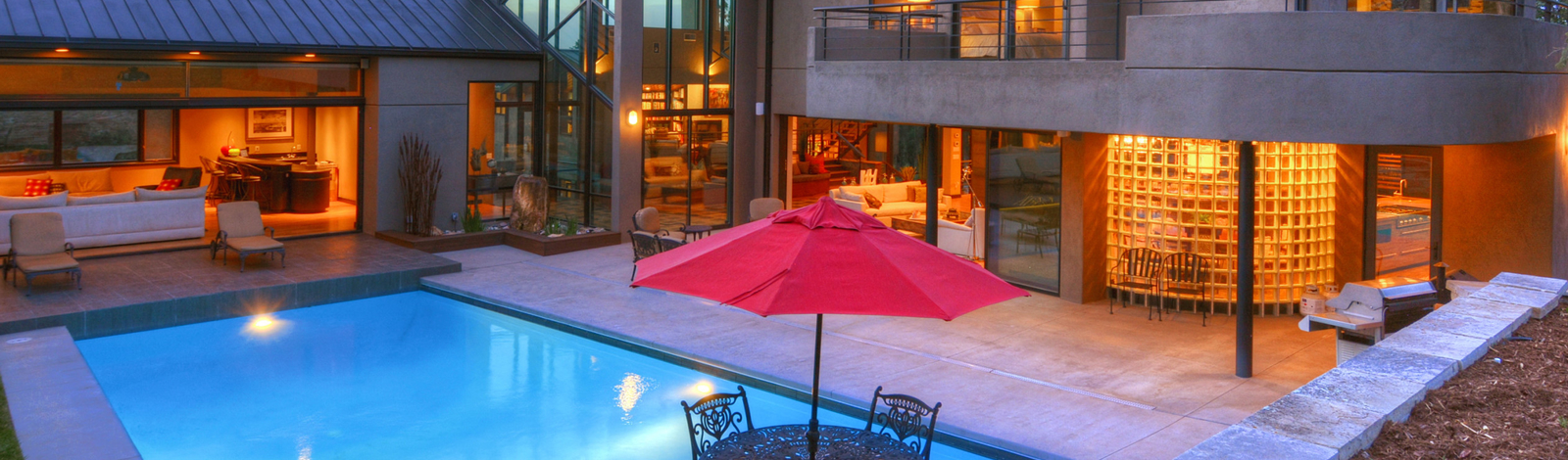 Outdoor living space of a luxury home in Colorado Springs. Blue pool, red patio umbrella, barbecue.