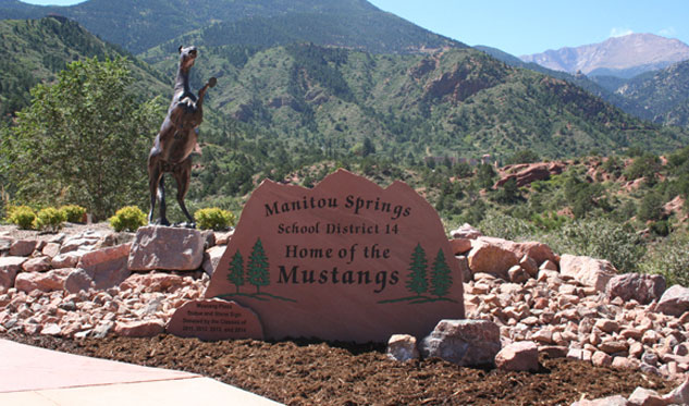 red rock sign of manitou springs school district 14 with horse statue and pikes peak in background